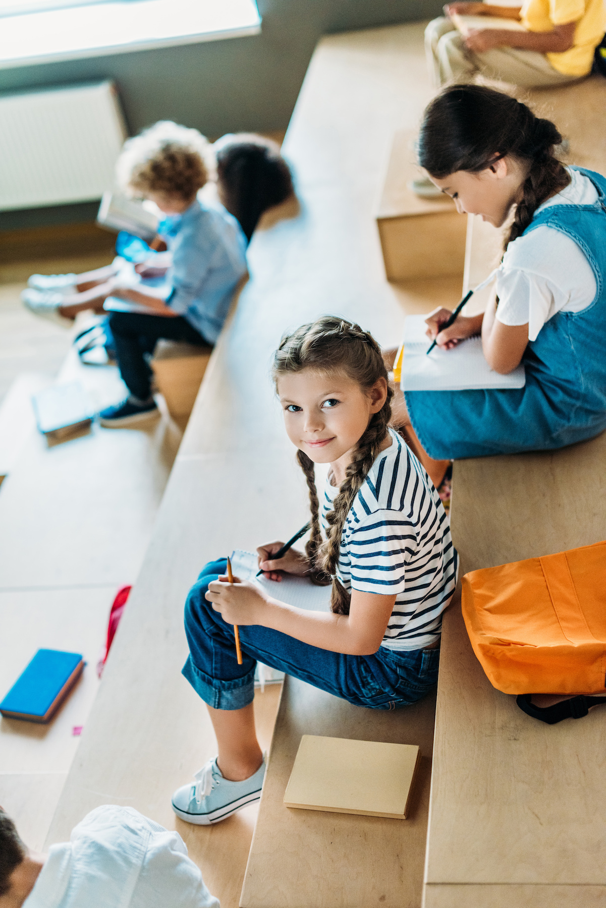 high angle view of schoolgirl with notebook studying on tribune at school corridor while her classmates sitting on background